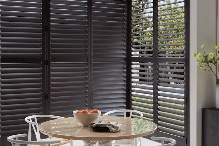 Dark plantation shutters with louvers tilted open beside a round dining table and white chairs