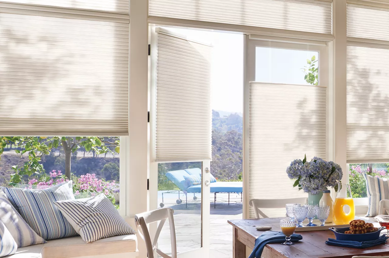Bright dining area with a wooden table set for breakfast, blue hydrangea centerpiece, and striped cushions, opening to a sunny patio.