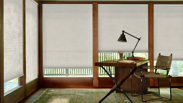 Honeycomb arizonashades - Pearl & Co Home office with a wooden desk and white honeycomb shades lowered evenly across a wall of windows