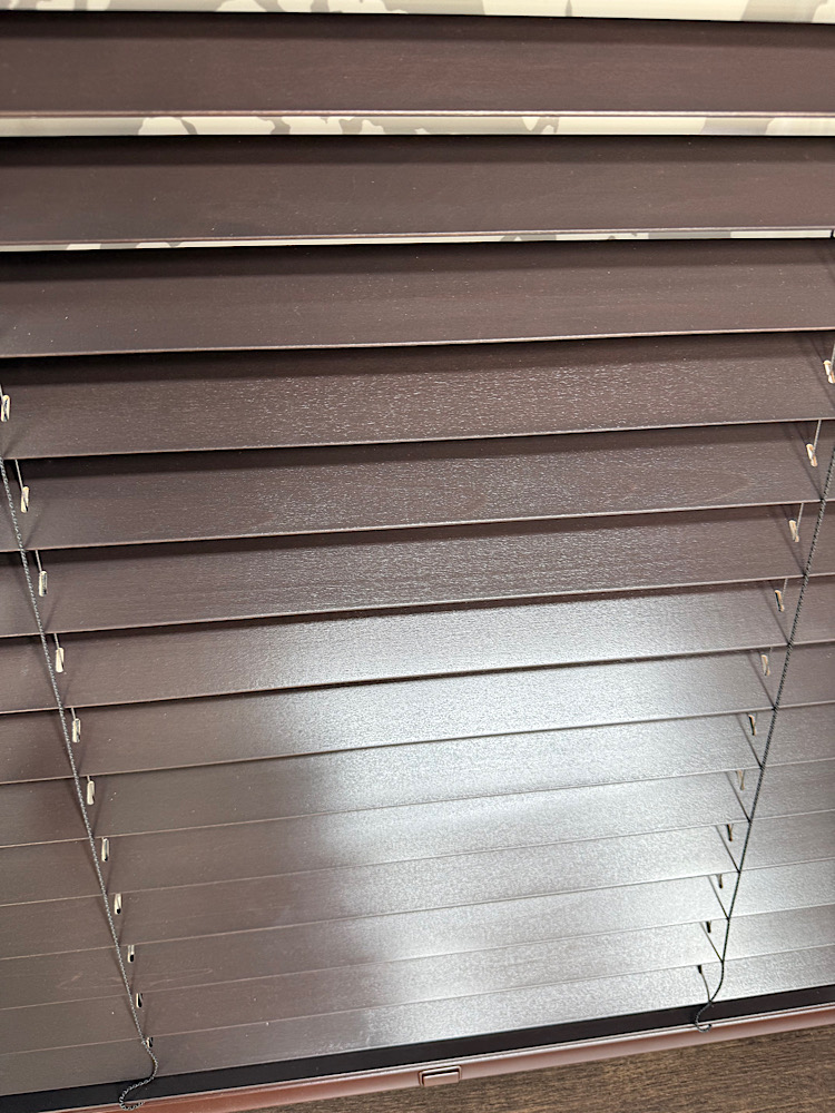 Brown horizontal window blinds closed over a window, with cords visible on the sides.