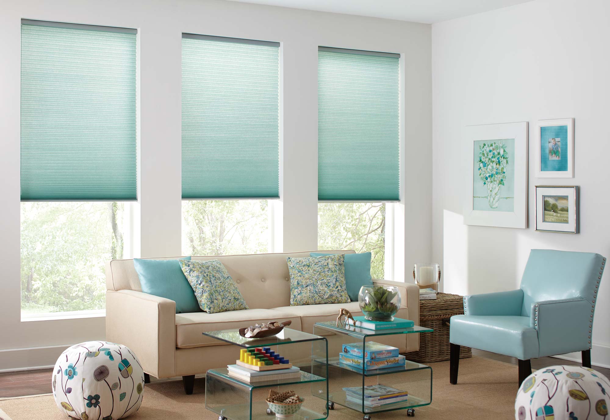 cellular-shades - Pearl & Co Three aqua cellular shades partly lowered over windows behind a cream sofa and a light blue armchair