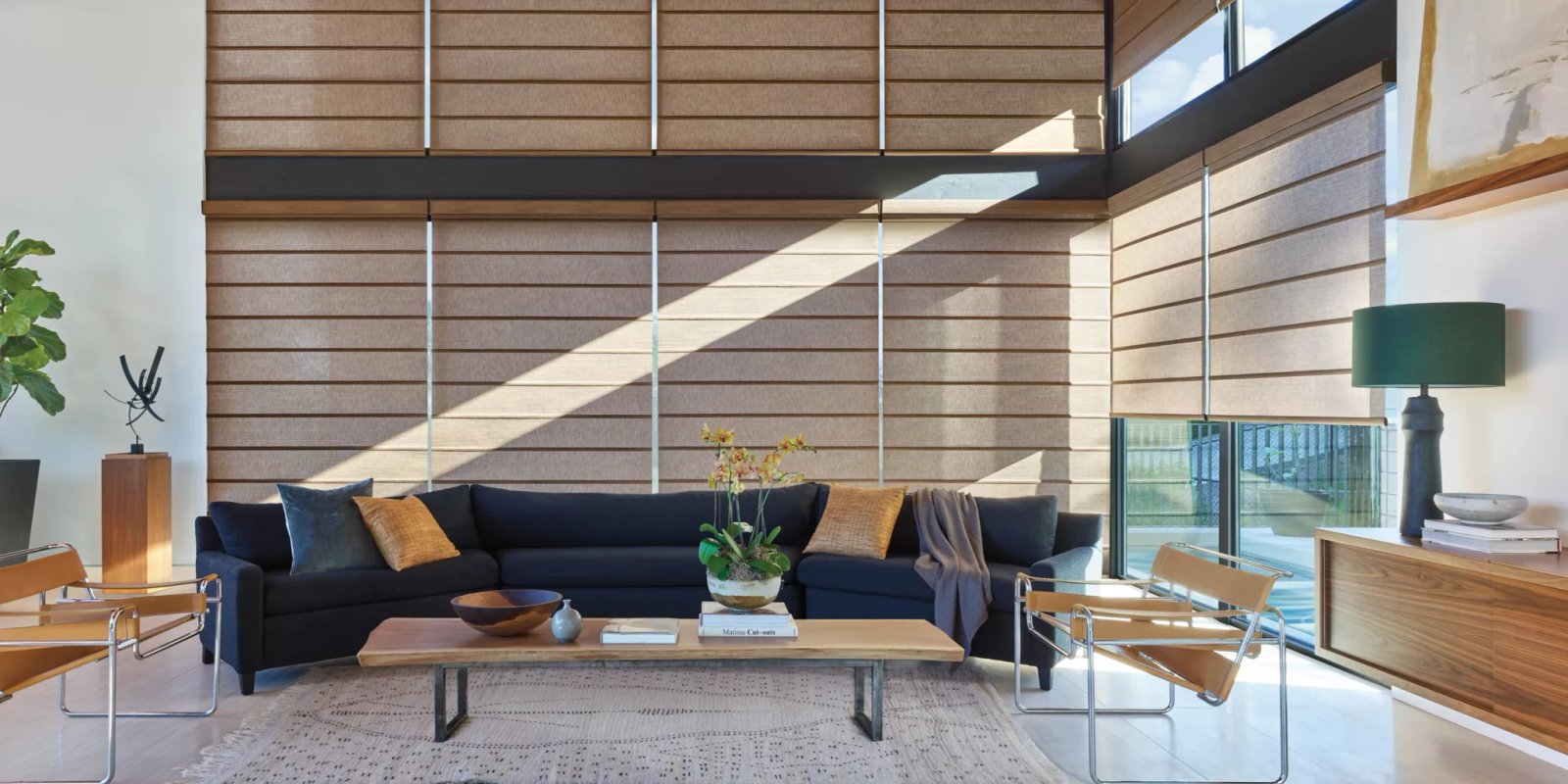 Roller shades in a living room - Pearl & Co Roller shades in a warm woven fabric covering tall two-story windows in a sunny modern living room