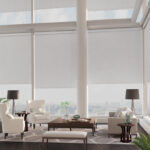 Light gray roller shades on tall corner windows in a bright modern living room with white furniture