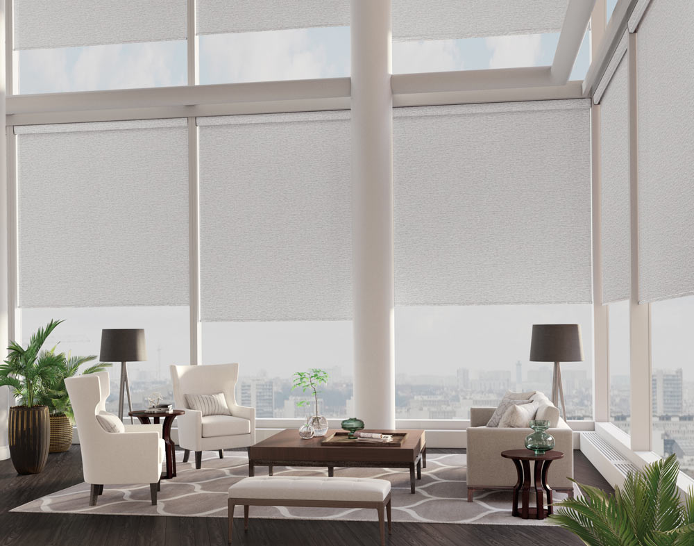 roller-shades - Pearl & Co Light gray roller shades lowered over tall corner windows in a bright living room with white armchairs
