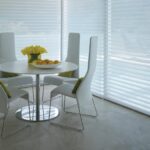 Window shadings on floor-to-ceiling windows around a white round dining table