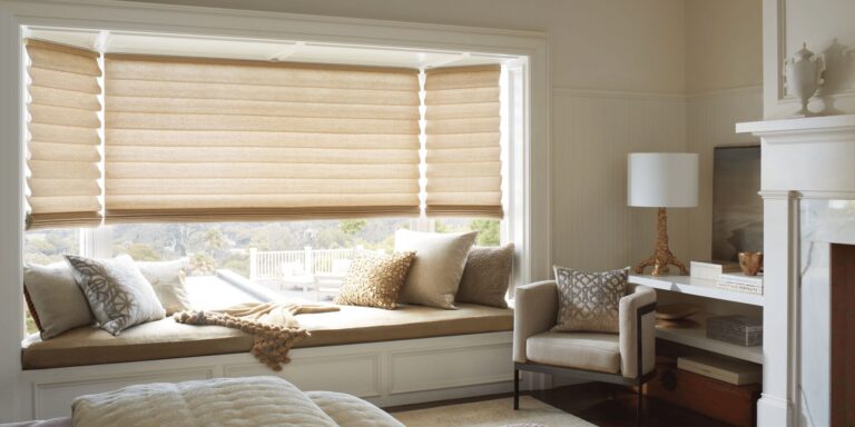 Vignette modern Roman shades in a warm neutral fabric across a bay window above a cushioned window seat