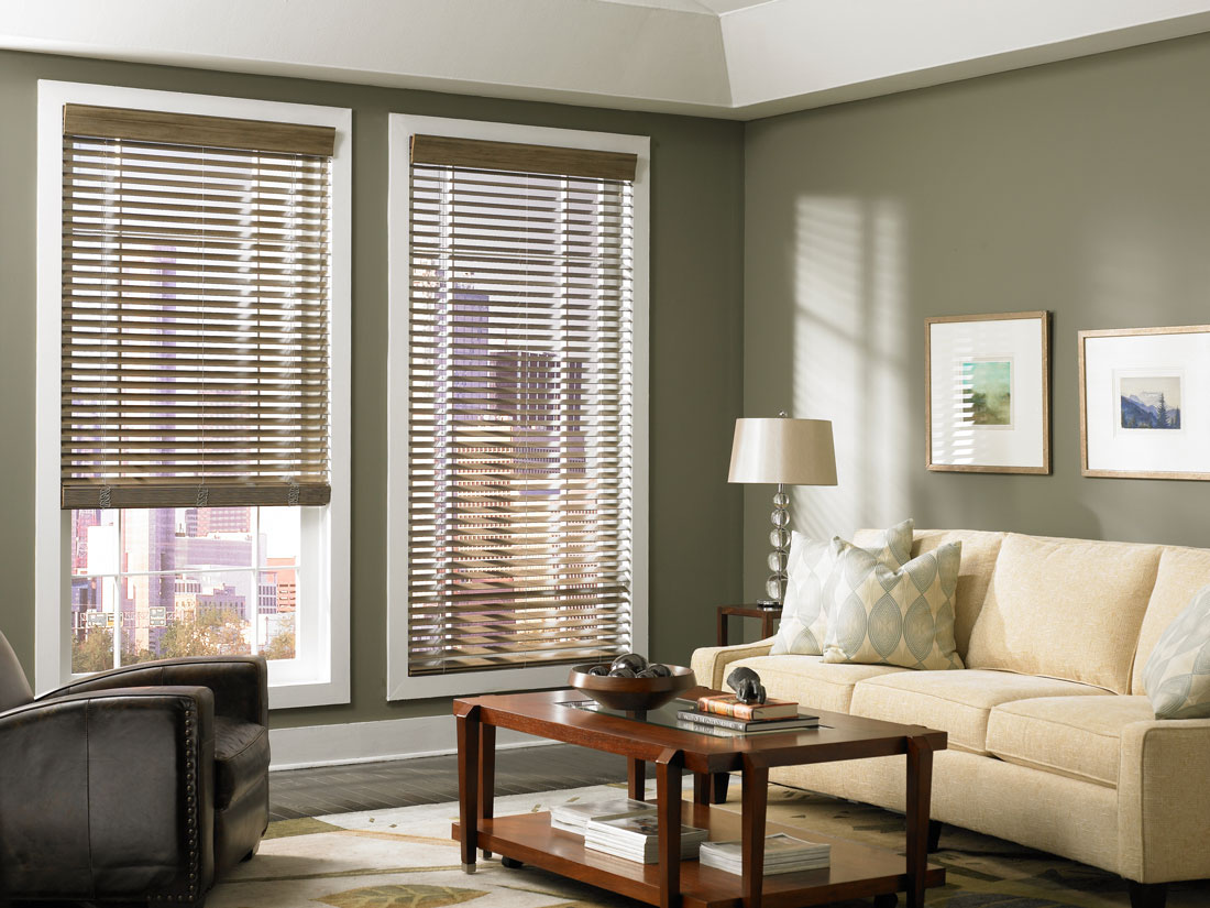 wood-blinds - Pearl & Co Tan wood blinds on two windows in a living room with green walls, a cream sofa and a wood coffee table